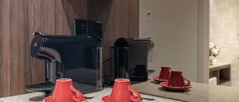 Una cocina con cafetera, dos tazas rojas sobre la encimera y un espejo que refleja la habitación.