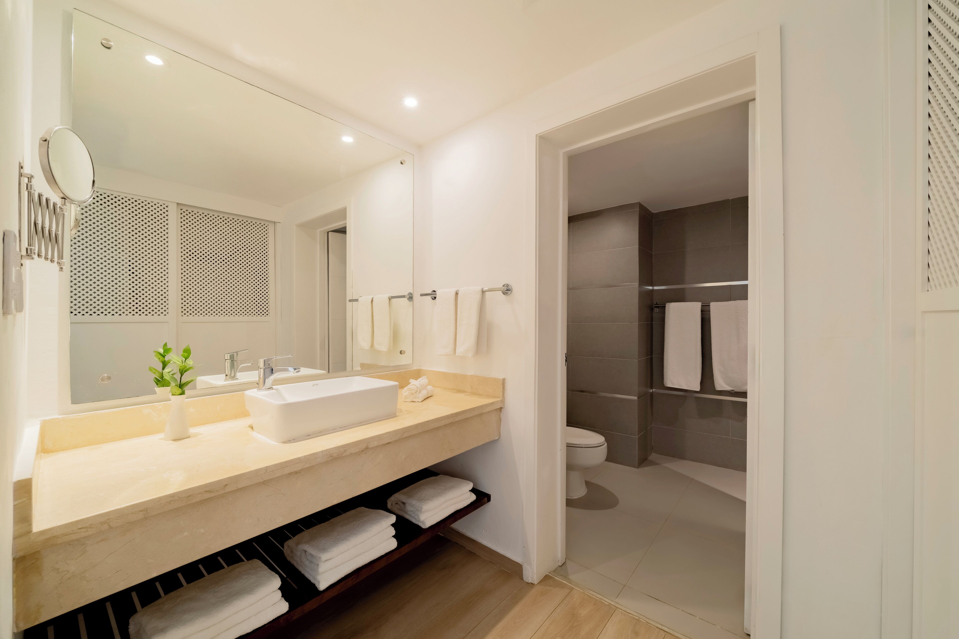 Un baño moderno con un espejo grande, un lavamanos, un inodoro y una zona de ducha.