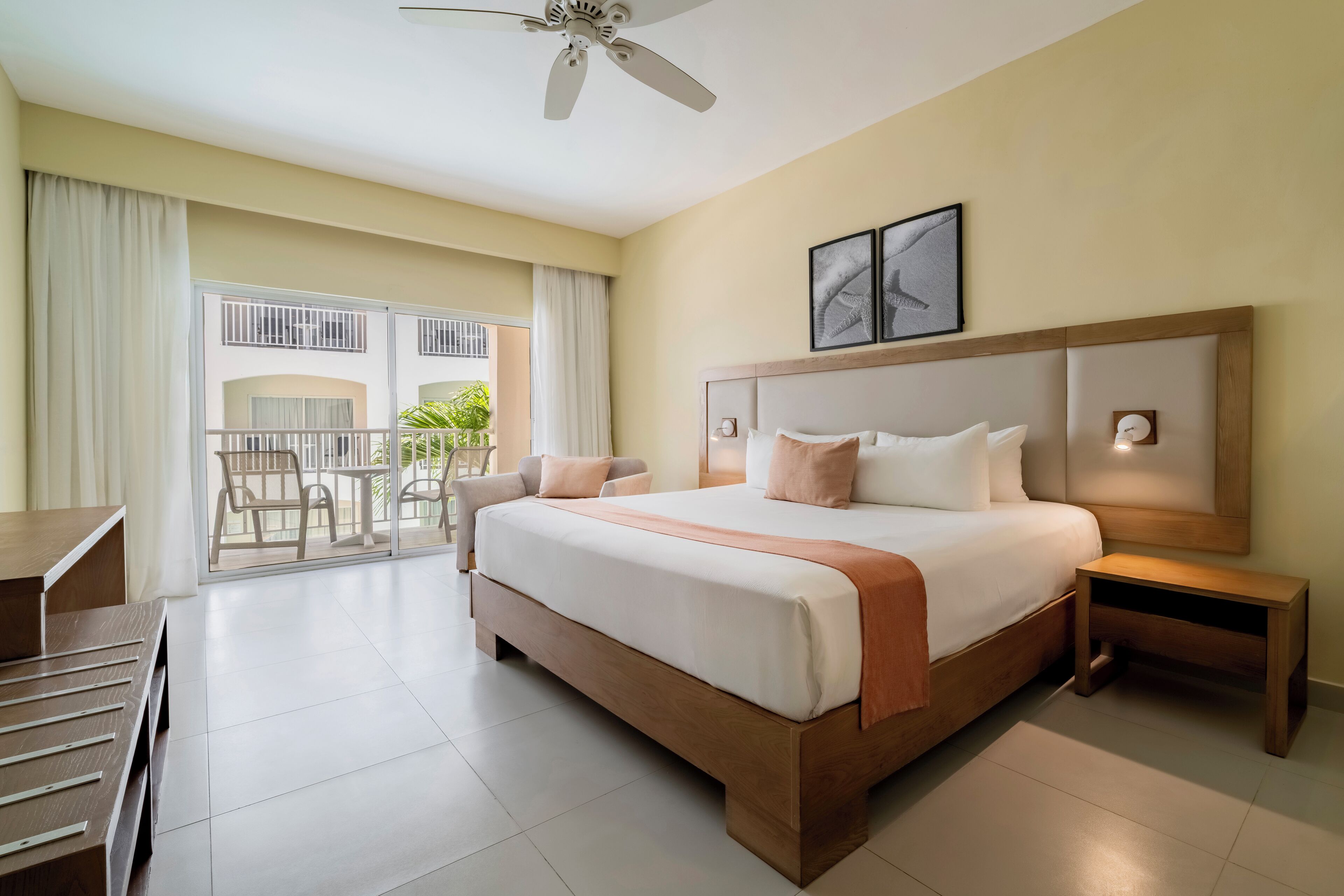 A hotel room with a large bed, a desk, a chair, a nightstand, and a ceiling fan.
