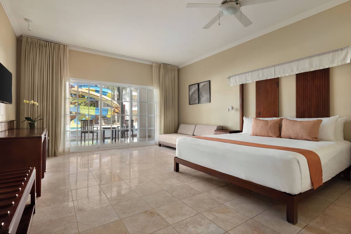 Habitación de hotel con una cama grande, televisión, escritorio y balcón con vistas a un parque acuático.