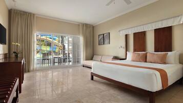 Habitación de hotel con cama, televisor, ventilador de techo, puerta corrediza a un balcón y vista a un parque acuático.