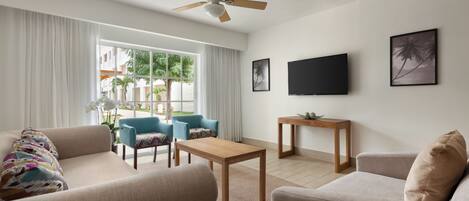 Un salon moderne doté d’un ventilateur de plafond, d’un téléviseur à écran plat et d’une grande fenêtre avec des rideaux.