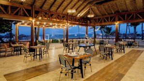 A restaurant with wooden tables and chairs, large windows, and a view of the ocean.