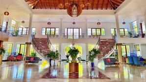 A spacious lobby with a high ceiling, large windows, and a central staircase.