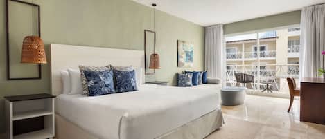 Habitación de hotel con una cama grande, ventilador de techo, balcón con vista al edificio y un escritorio con silla.