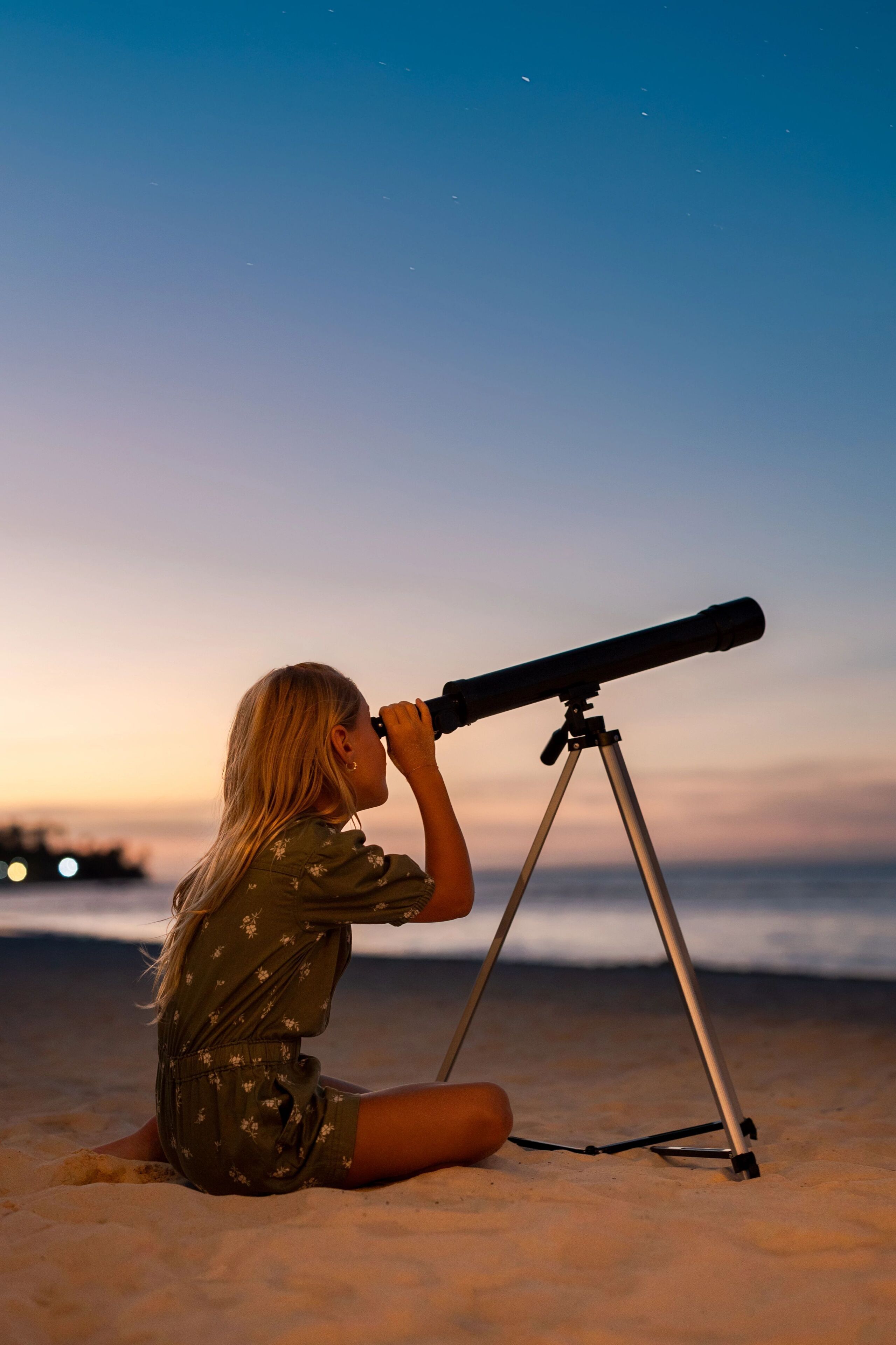A person using a telescope on a sandy beach at sunset.