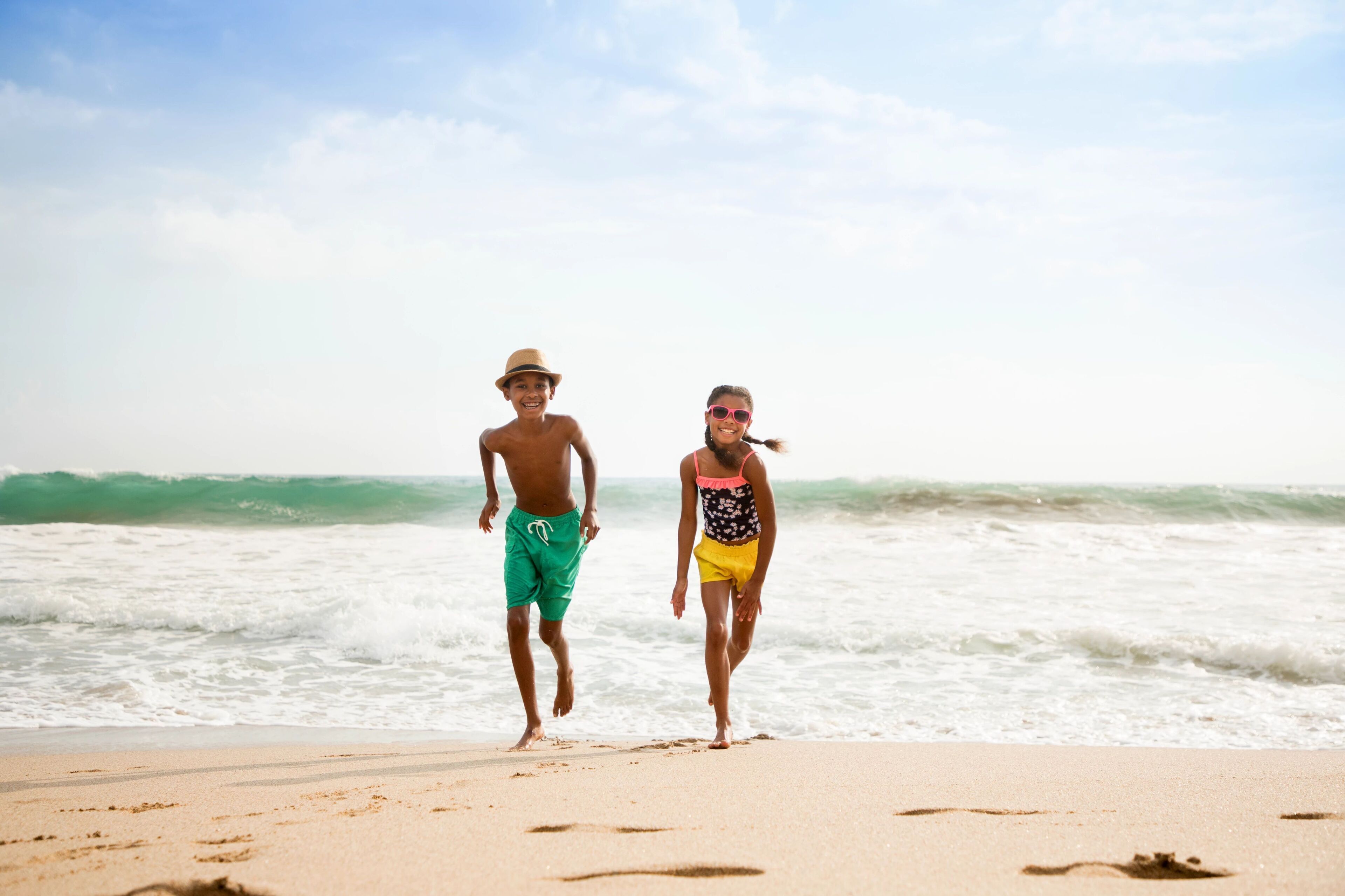 Dos personas caminando sobre una playa arenosa con olas al fondo.