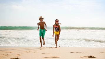 Dos personas caminando sobre una playa arenosa con olas al fondo.