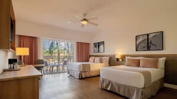 Habitación de hotel con dos camas, un escritorio, una silla, un ventilador de techo y un amplio ventanal con vistas.