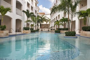 A swimming pool with a tiled edge, surrounded by white buildings with balconies and palm trees.