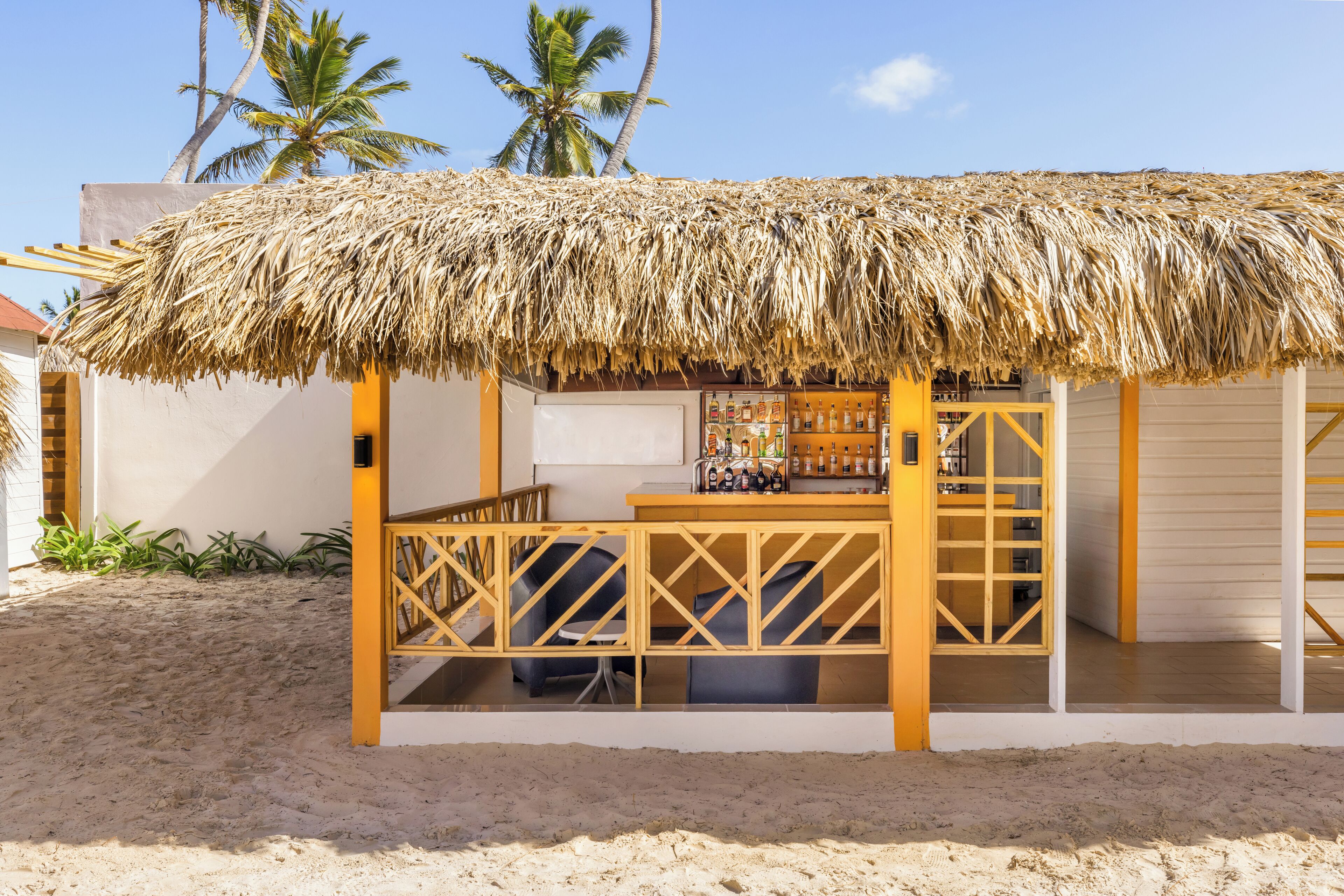 Un petit chalet situé au bord de la plage, doté d’un toit de chaume, de meubles en bois et d’un espace bar.