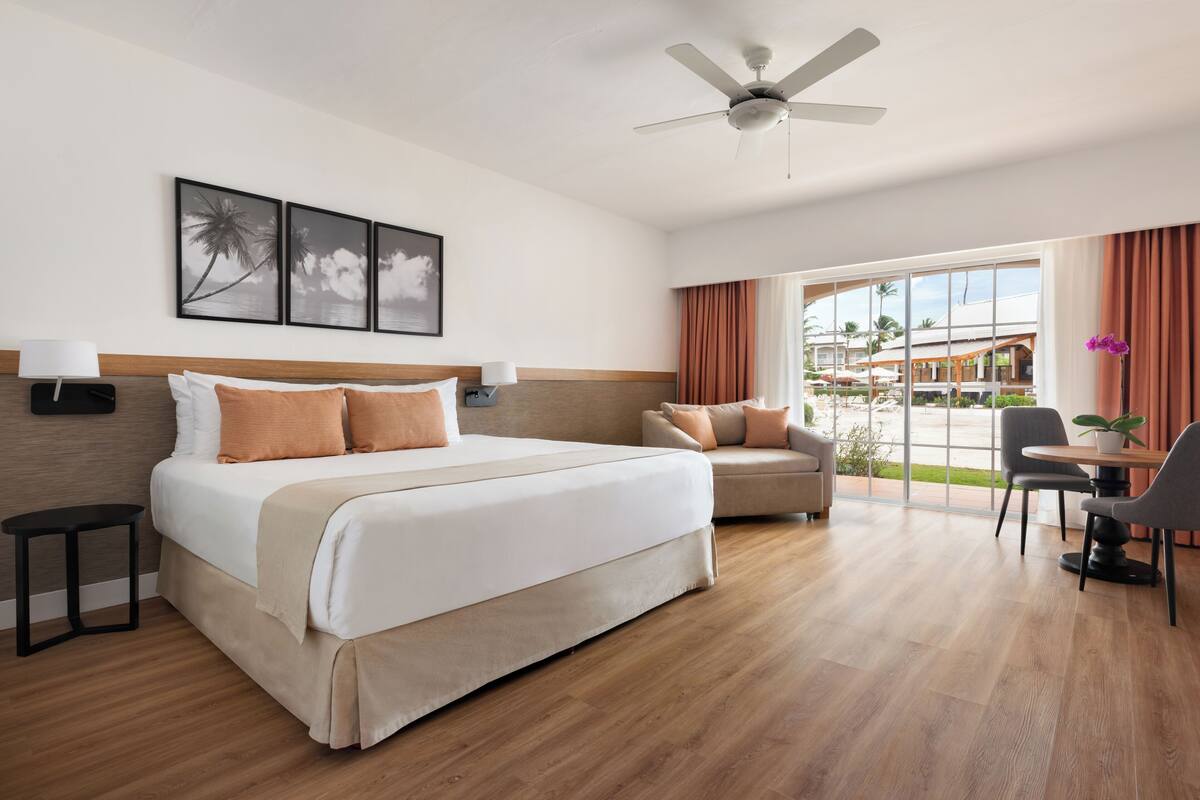 Habitación de hotel con cama, sofá, mesa de comedor, ventilador de techo y vistas al exterior.