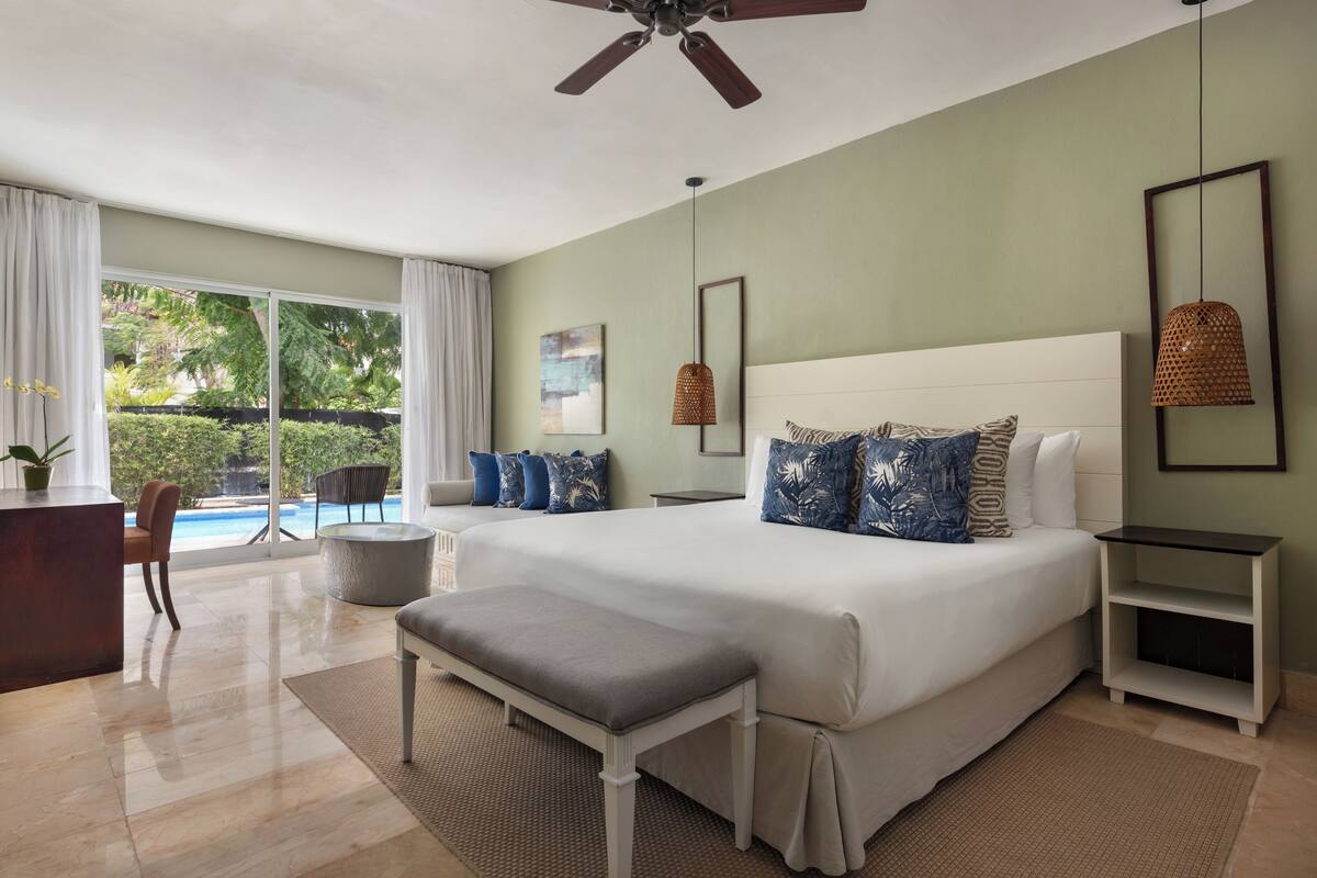 Un dormitorio amplio con una cama grande, un escritorio y vistas a una piscina.