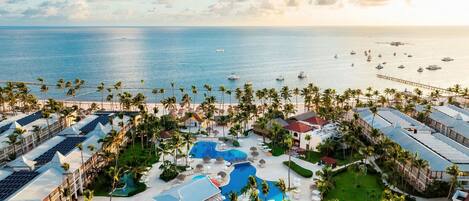 A resort with multiple swimming pools, a beach area, and a view of the ocean with boats.