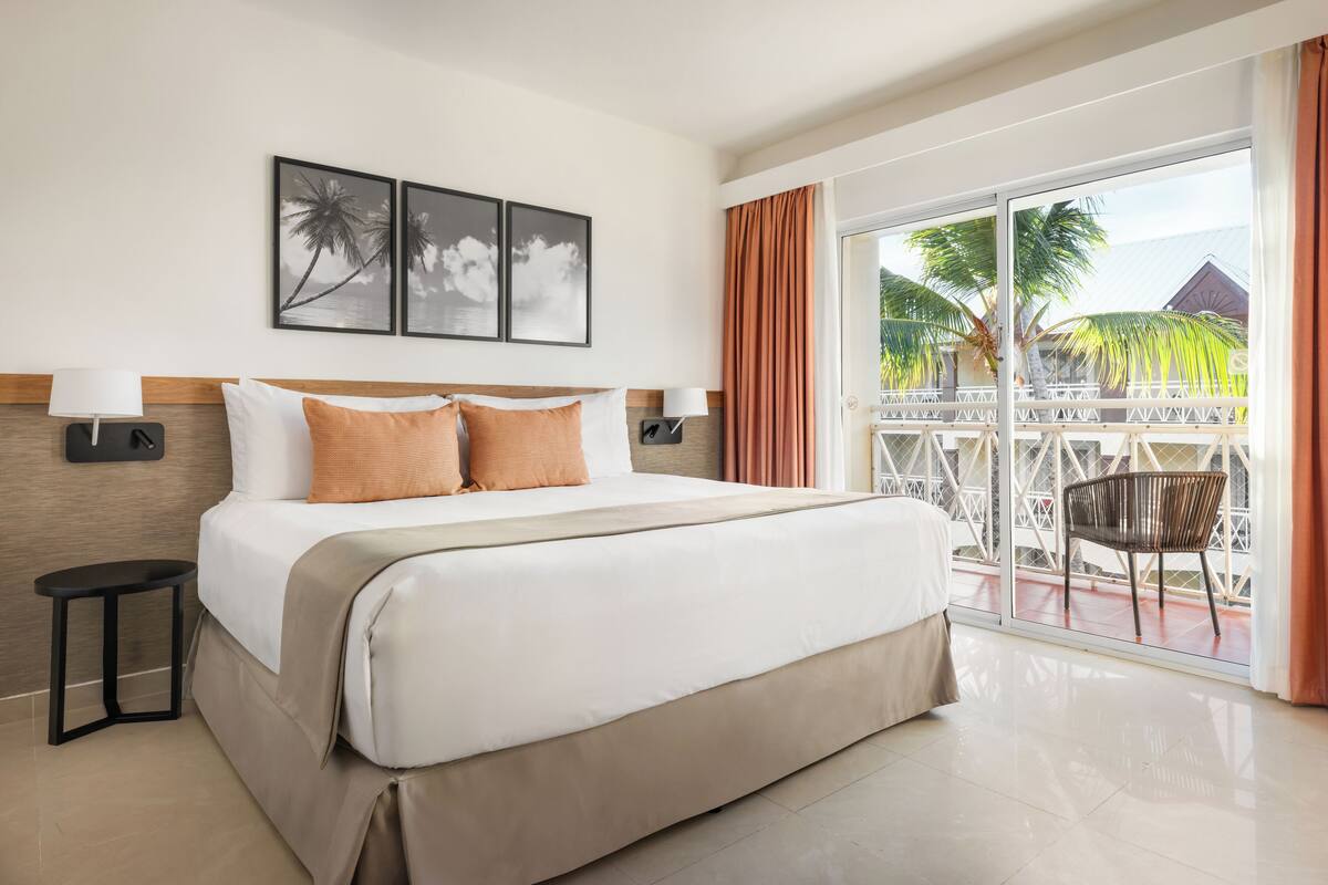 Habitación de hotel con una cama grande, dos lámparas de pared, una mesita pequeña y un balcón con una silla.
