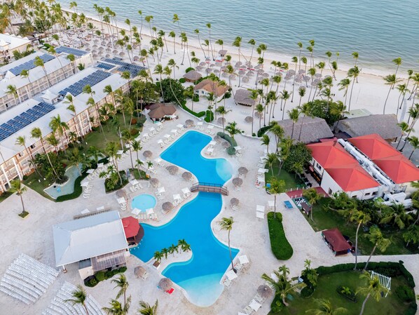 An aerial view of a resort with a large swimming pool, palm trees, and beach umbrellas. - Sunscape Coco Punta Cana - All Inclusive (Punta Cana)