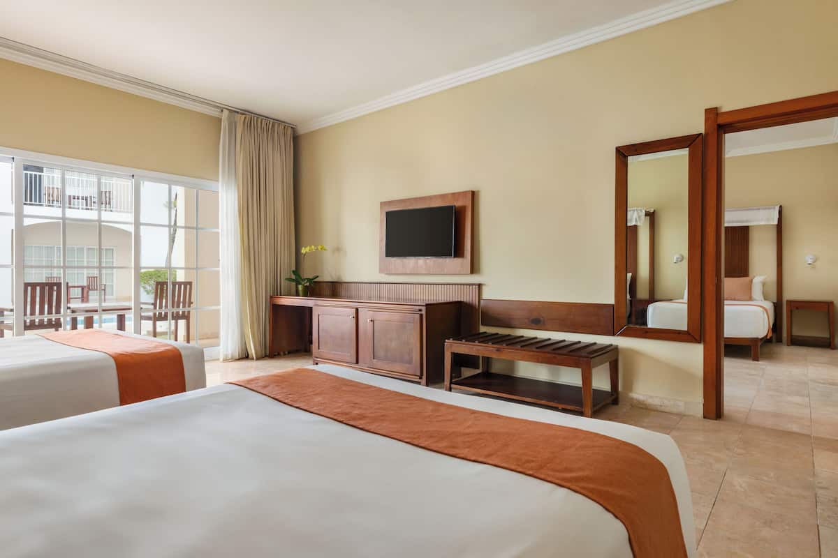 Habitación de hotel con dos camas, televisión, escritorio y ventana grande.
