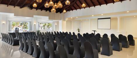 A conference room with rows of chairs, a stage, and a large screen.