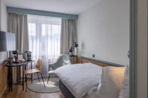 A hotel room with a bed, a desk with a chair, a TV, and a window with curtains.