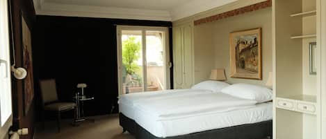 A bedroom with a bed, a chair, a small table, and a painting on the wall.