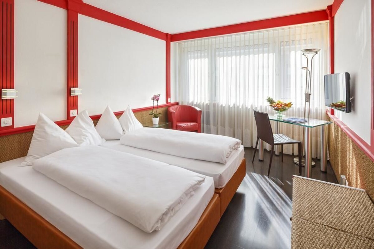 Habitación de hotel con dos camas, un escritorio, una silla, un televisor y una ventana con cortinas.
