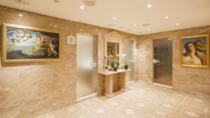 A luxurious bathroom with marble walls, a vanity with a mirror, and two framed paintings. - Hotel Luzernerhof (Lucerne)