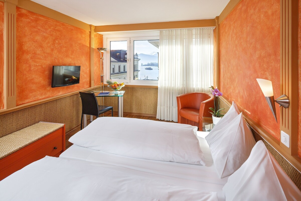A hotel room with a bed, a desk, a chair, a TV, and a window with a view of a body of water.