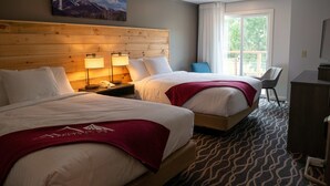 Habitación de hotel con dos camas, cabecero de madera, un escritorio y ventana con vistas a zonas verdes.