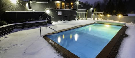 A swimming pool surrounded by snow, with a building in the background.