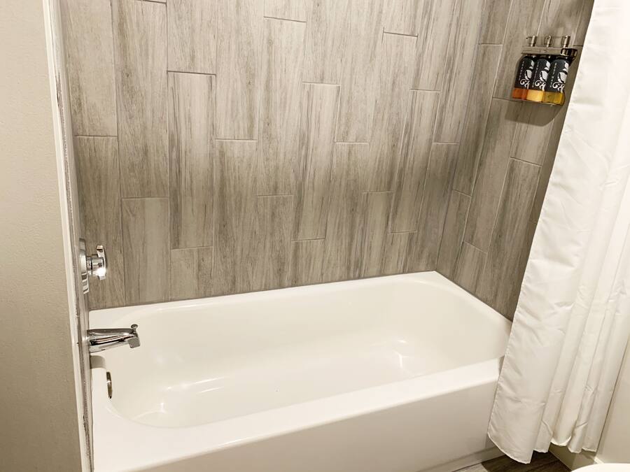 A bathroom with a wooden wall, a white bathtub, and a shelf with toiletries.