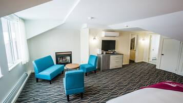 A hotel room with a high ceiling, a large bed, a blue sofa, a small table, and a kitchenette area.