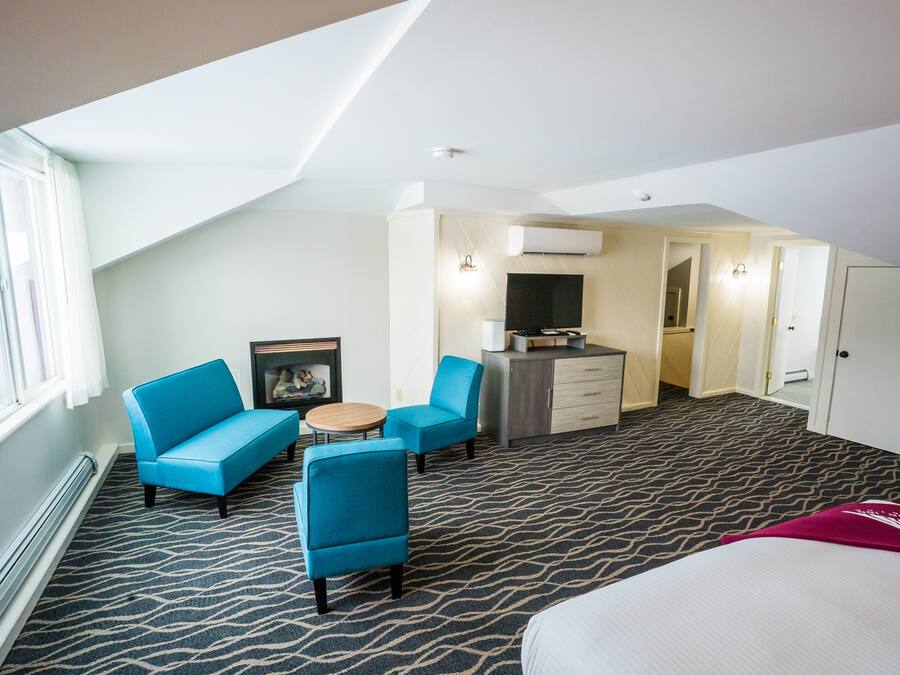 A hotel room with a high ceiling, a large bed, a blue sofa, a small table, and a kitchenette area.