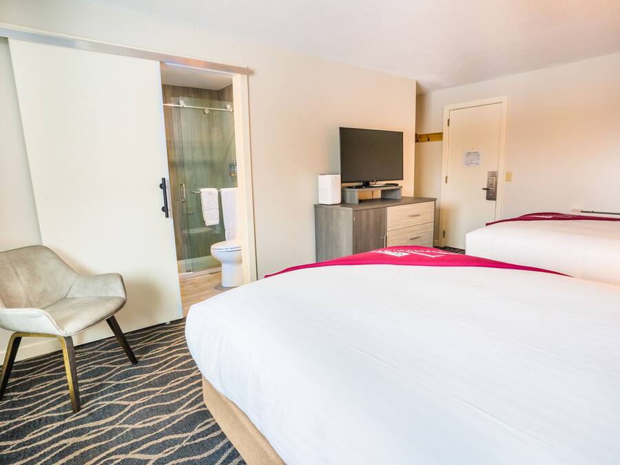 Une chambre d’hôtel avec un lit, une chaise, un bureau avec une télévision et une salle de bain visible à travers une porte ouverte.