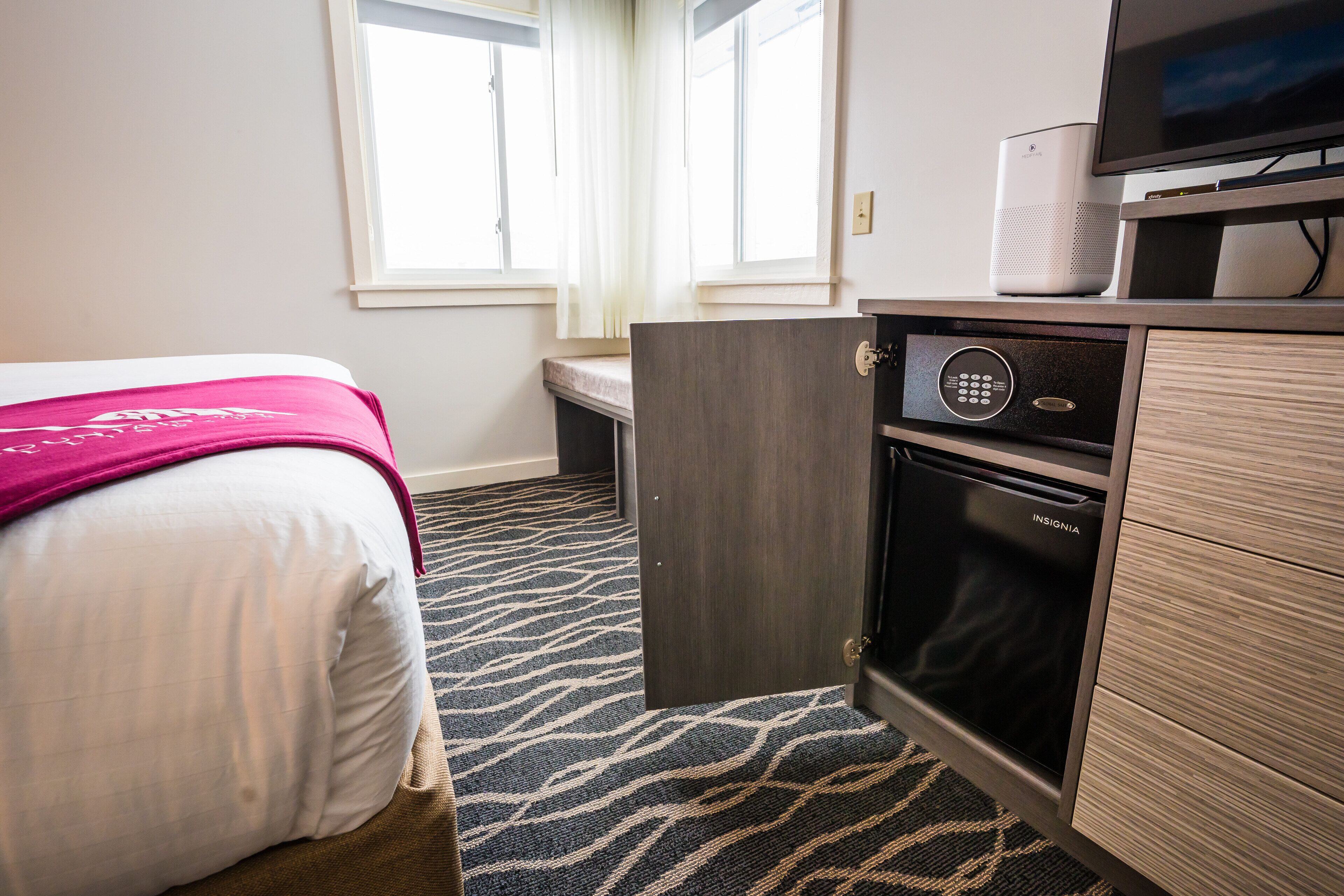A hotel room with a bed, a television, a minibar, and a door leading to a bathroom.