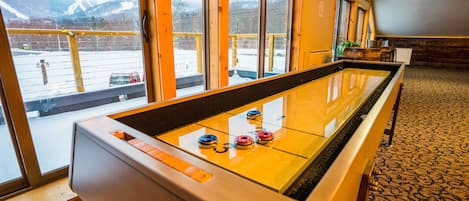 Una habitación con mesa de futbolín, ventanas amplias que dan a un paisaje nevado y piso alfombrado.