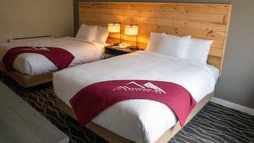 Habitación de hotel con dos camas, cada una con cabecero de madera, ropa de cama blanca y una manta roja con el logotipo del hotel. Hay dos lámparas de noche y un cuadro en la pared sobre las camas.