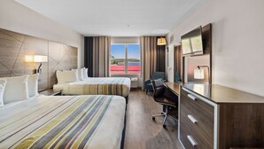 A hotel room with two beds, a desk, a chair, a TV, and a window with a view of a red building. - Country Inn & Suites by Radisson, Myrtle Beach, SC (Myrtle Beach)
