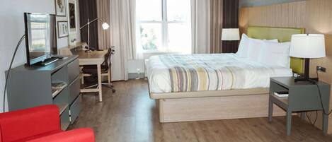 Habitación de hotel con cama, escritorio, silla, televisor y sofá rojo.