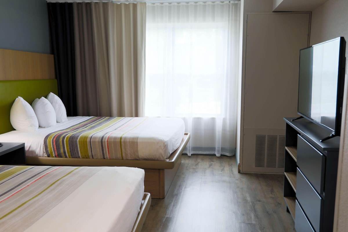 A hotel room with two beds, a television, and a window with curtains.