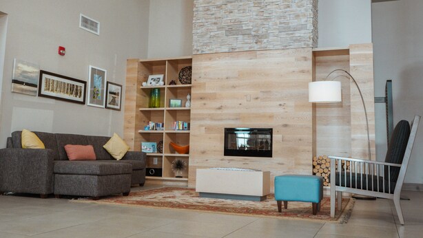 A modern living room with a fireplace, a grey sofa, a bookshelf, and a blue ottoman. - Country Inn & Suites by Radisson, Myrtle Beach, SC (Myrtle Beach)