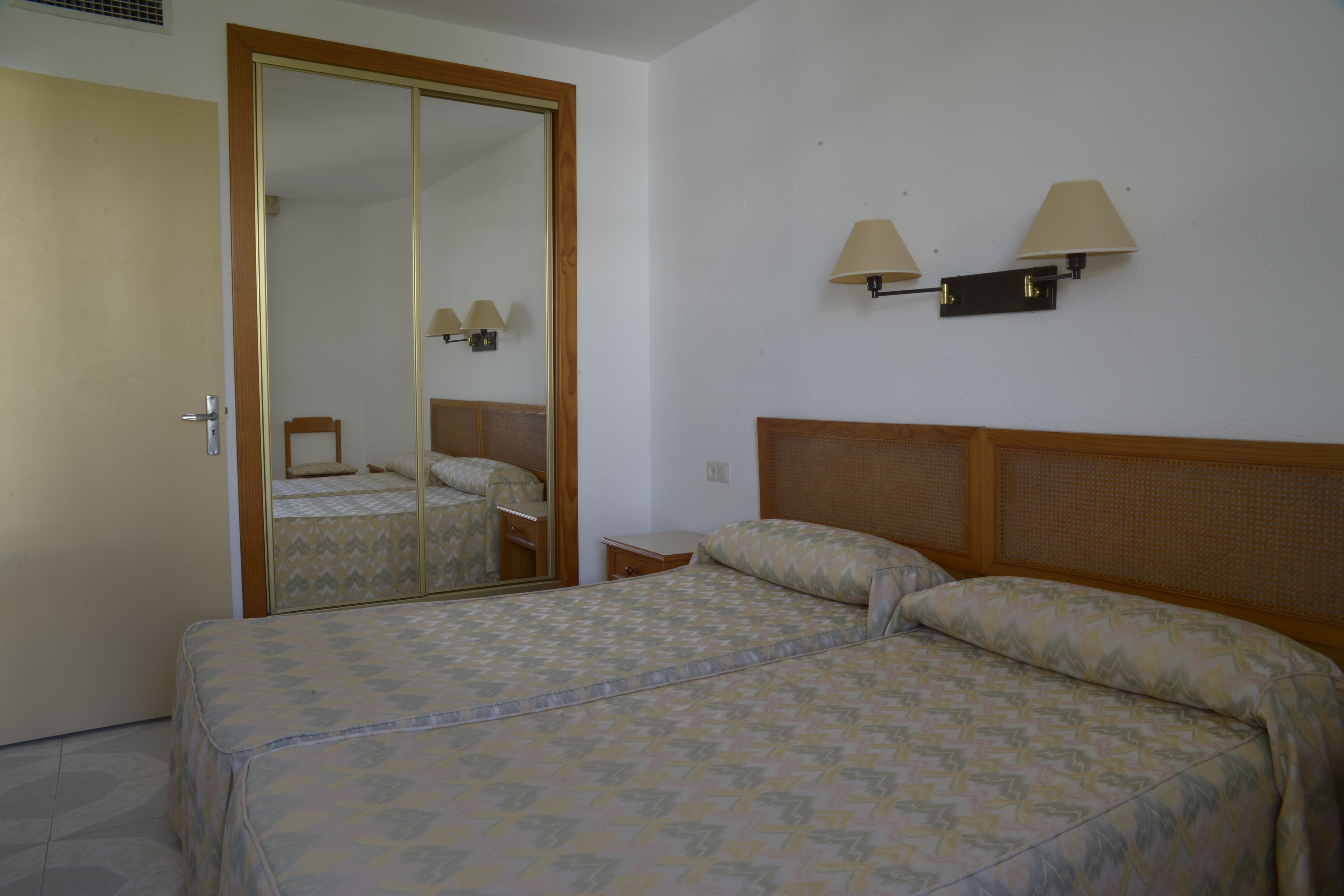 Een slaapkamer met een bed, een spiegel, een kledingkast en twee wandlampen.