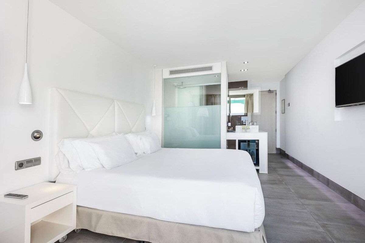 Una habitación de hotel moderna con una cama grande, una mesita de noche y un televisor fijado a la pared.