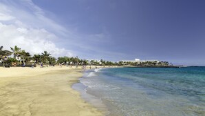 A beach with clear waters, palm trees, and a resort building in the background. - Barceló Teguise Beach - Adults only (Teguise)
