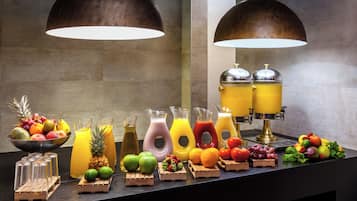 Um buffet de café da manhã com diversas frutas, sucos e uma máquina de café.