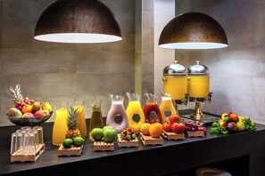 Un bufé de desayuno con varias frutas, jugos y una máquina de café.