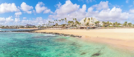 Un hotel costero con vista a la playa, aguas turquesas cristalinas y palmeras.
