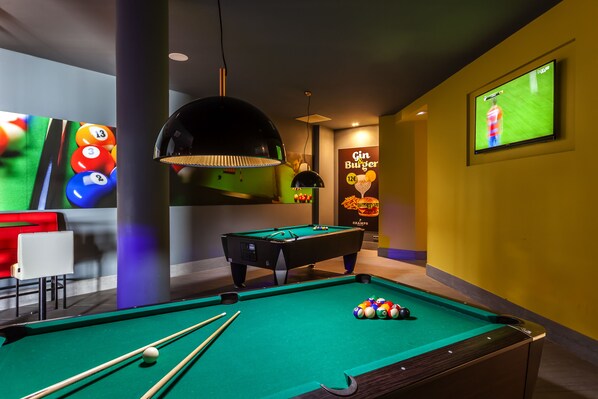A pool table with balls and cues, a television displaying a sports game, and a poster advertising a gin burger. - Barceló Teguise Beach - Adults only (Teguise)