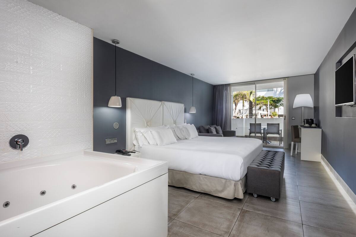 A modern hotel room with a large bed, a separate seating area, a small desk, and a bathtub.