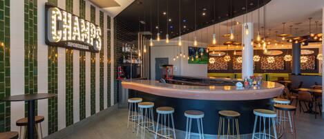 A sports bar with a curved bar, multiple stools, and a variety of hanging lights.