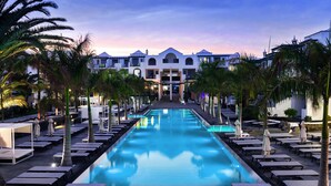 A pool area with lounge chairs and umbrellas, surrounded by palm trees, leading to a building with multiple balconies. - Barceló Teguise Beach - Adults only (Teguise)